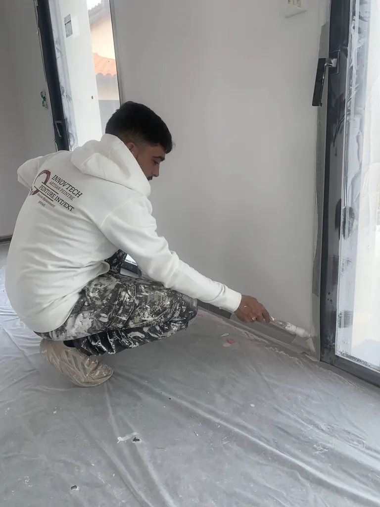 Artisan peintre INNOV'TECH 66 en tenue de travail réalisant des finitions de plinthes sur un chantier
